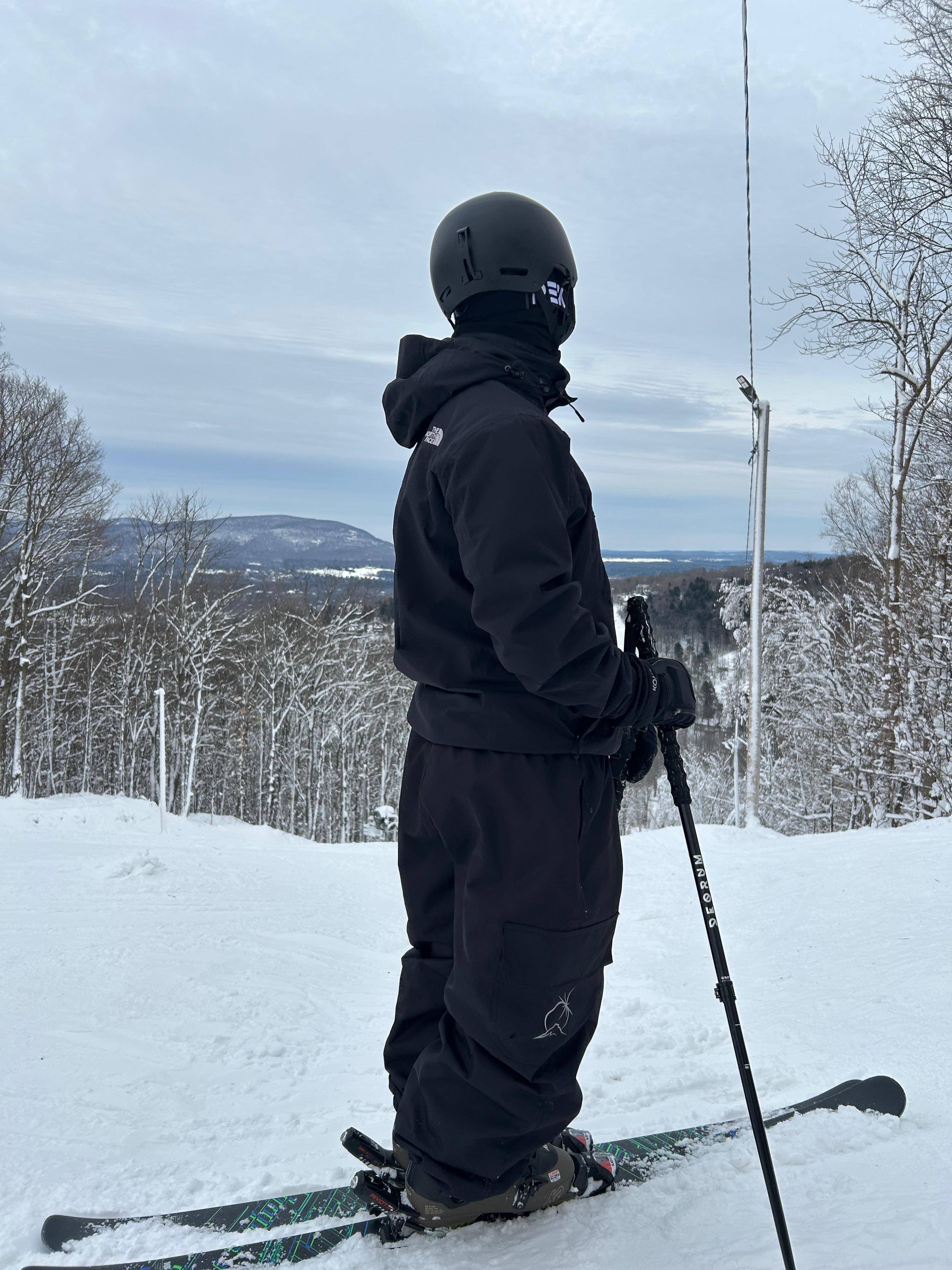 Person in black baggy snow pants standing on a snowy slope with skis and poles.