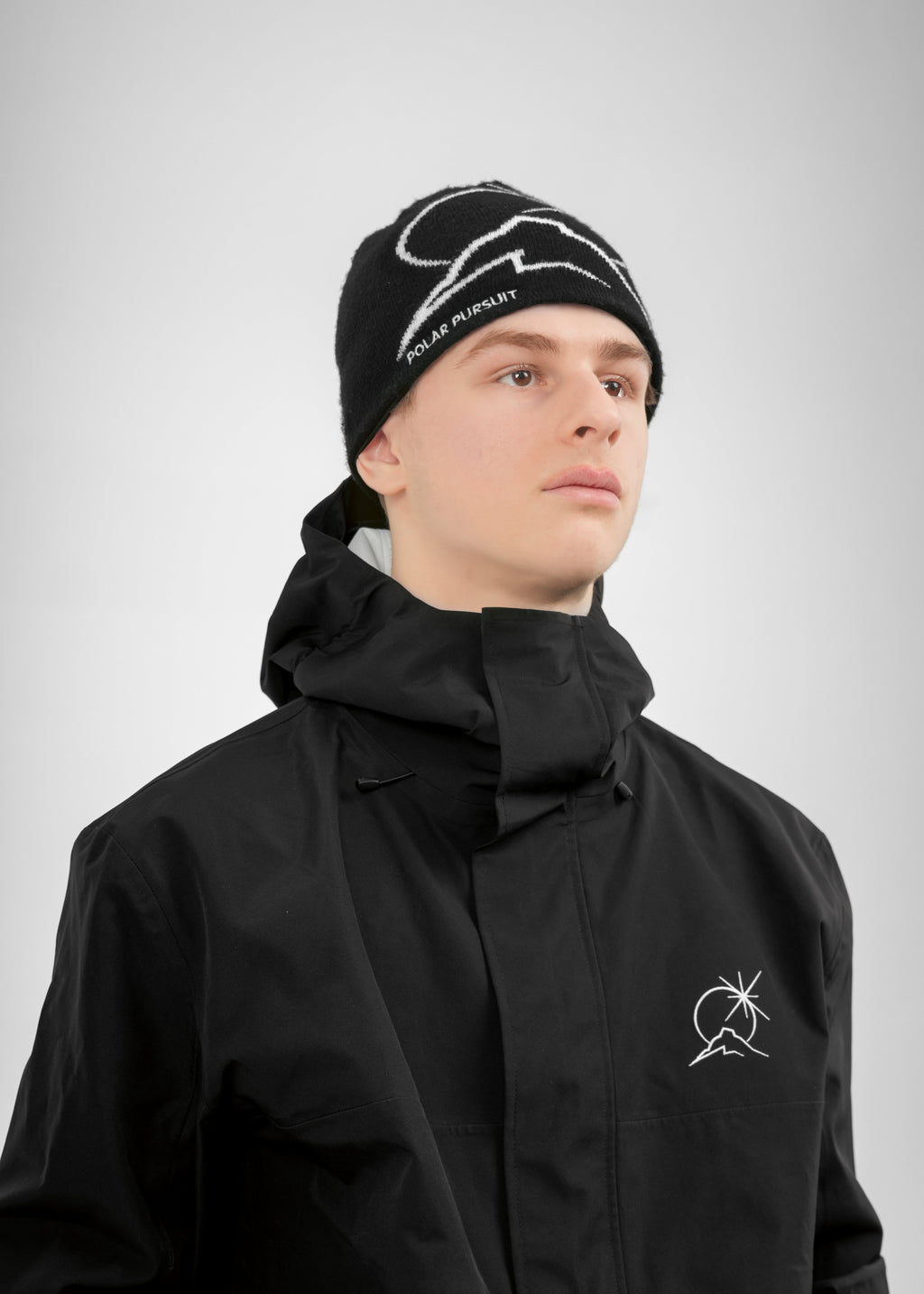 Person wearing a black Polar Pursuit jacket and Polar Pursuit beanie with visible branding on a gray background