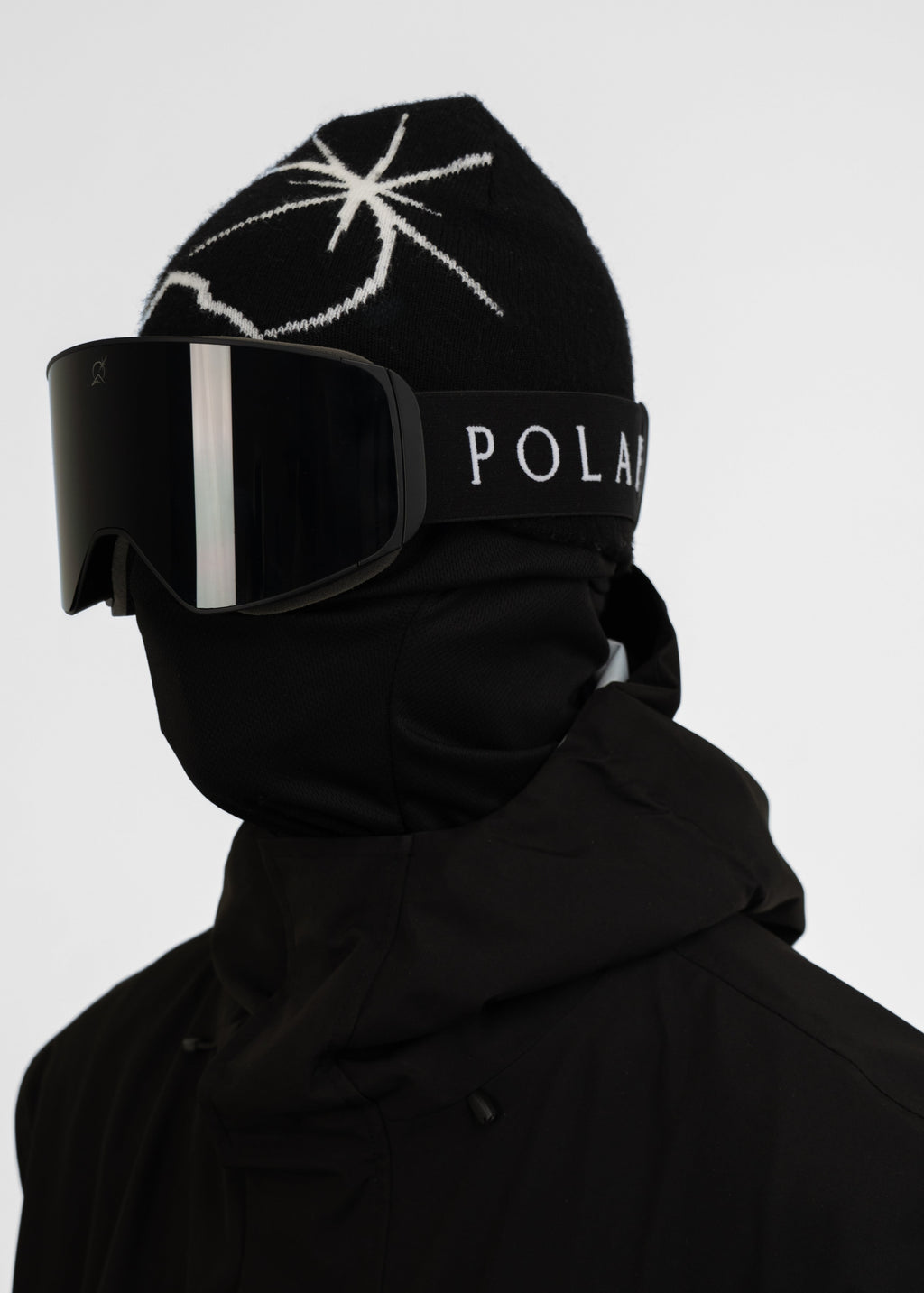 Person wearing a black Polar Pursuit beanie with a white logo and black Polar Pursuit goggles with 'Polar Pursuit' branding on a light gray background.