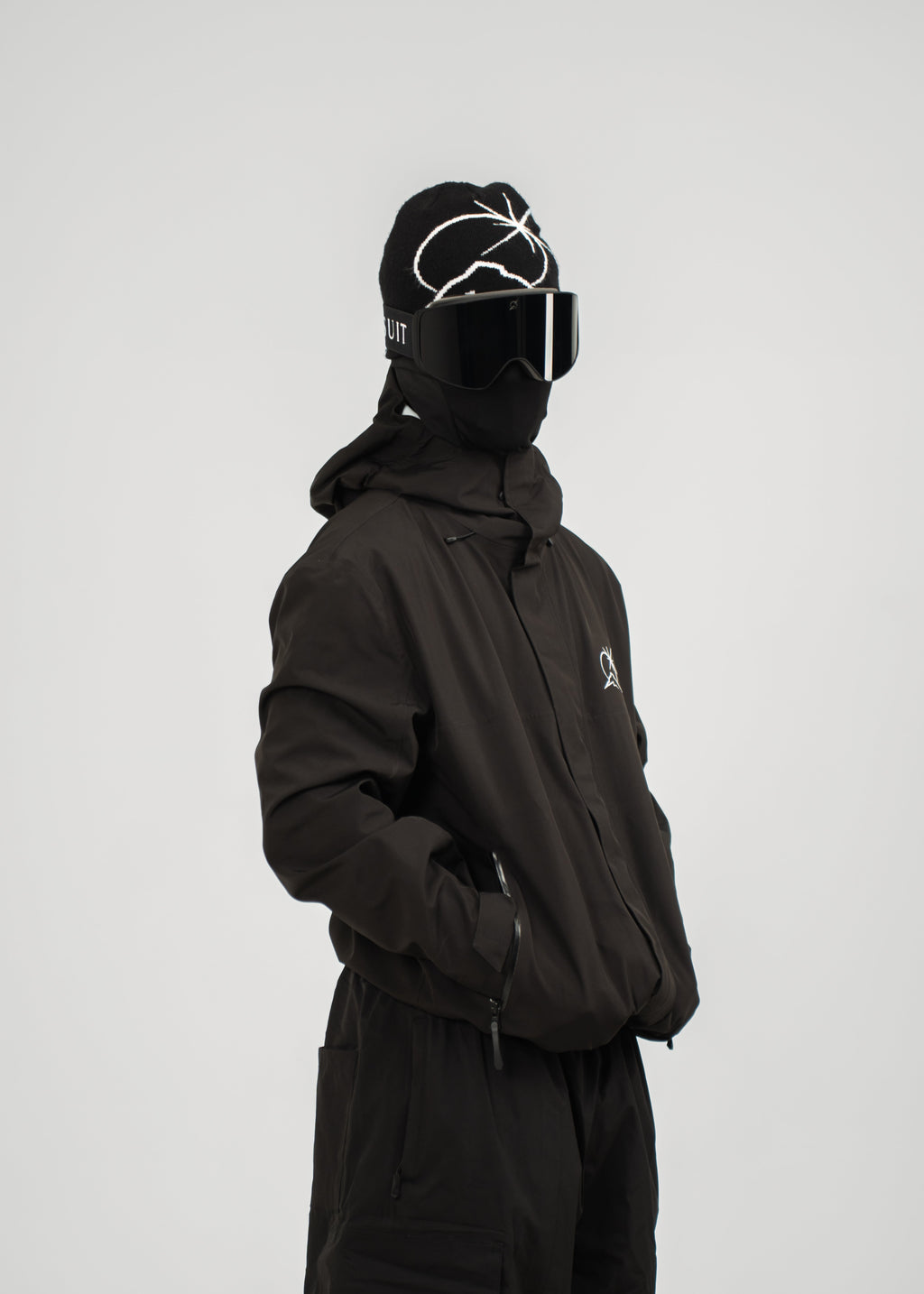 Person wearing a black polar pursuit snowsuit and helmet with goggles on a white background