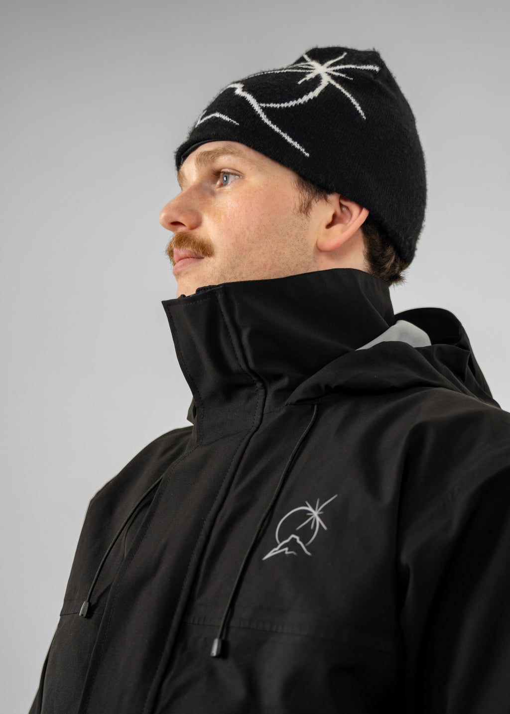 Person wearing a black Polar Pursuit jacket and Polar Pursuit beanie with white patterns on a gray background