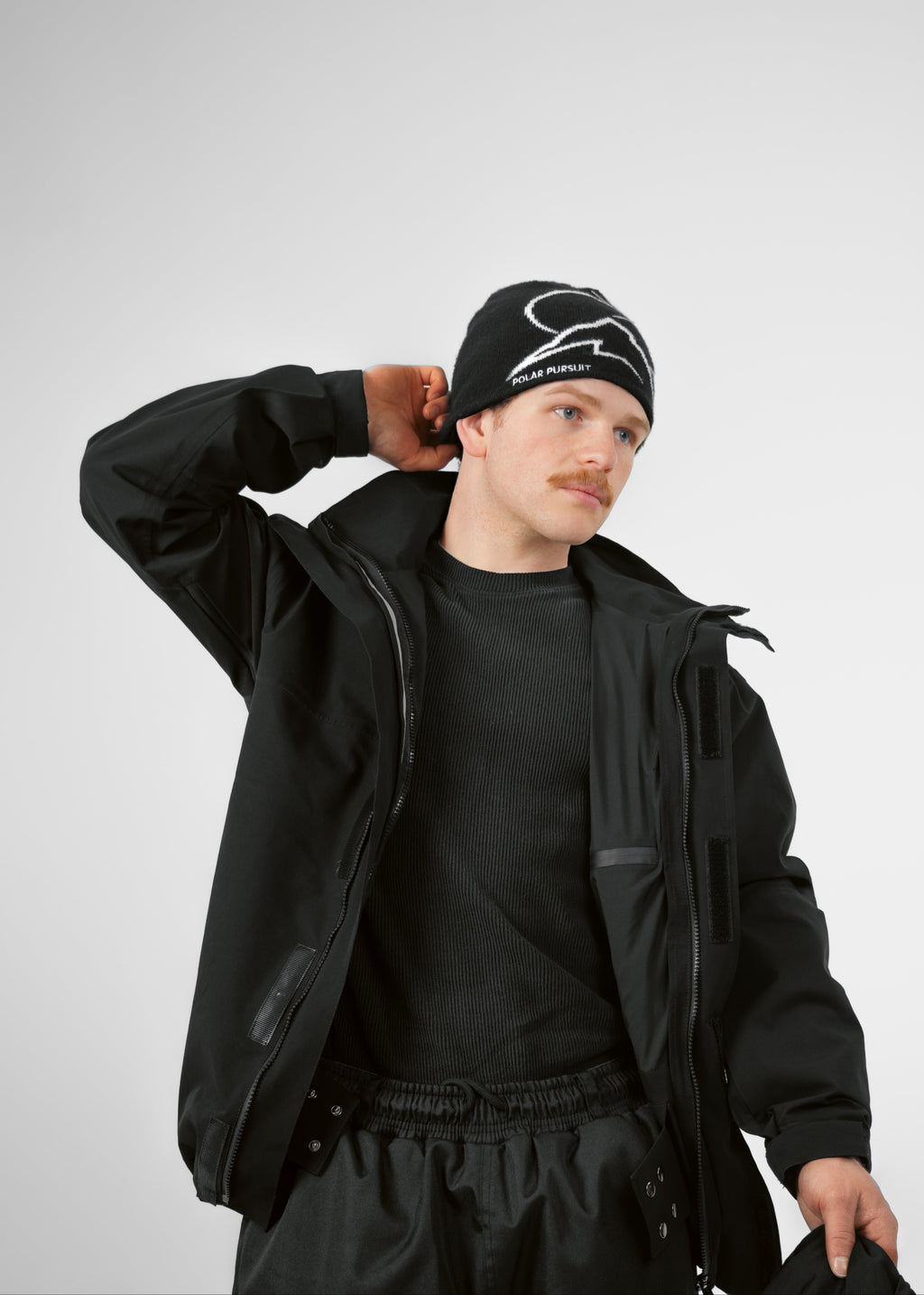 Person wearing a black Polar Pursuit outfit with a Polar Pursuit cap on a light gray background