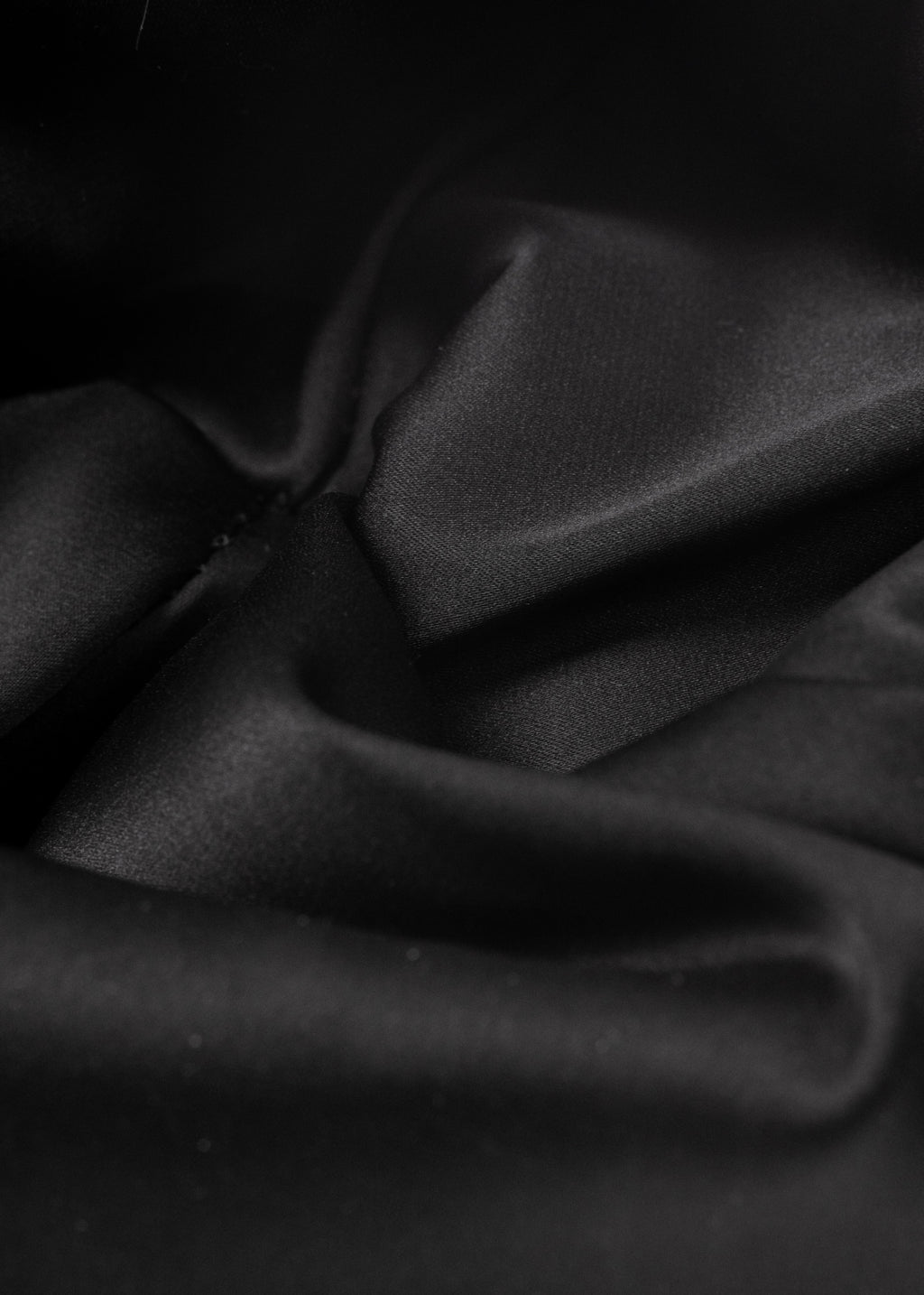 Close-up of a satin fabric of a black Polar Pursuit beanie with folds on a black background