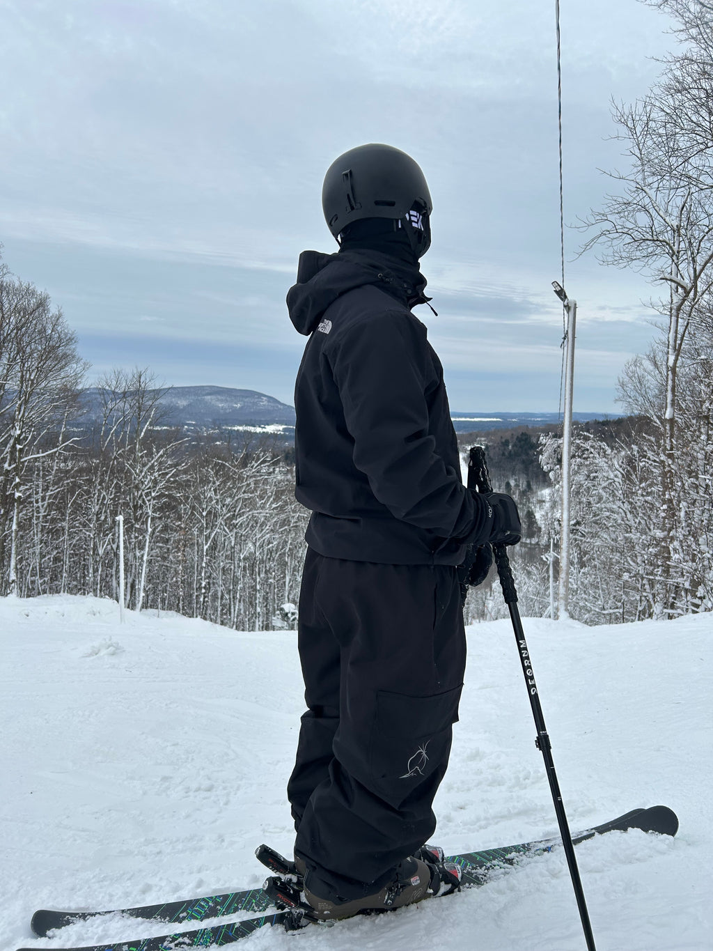 Person in black baggy snow pants standing on a snowy slope with skis and poles.