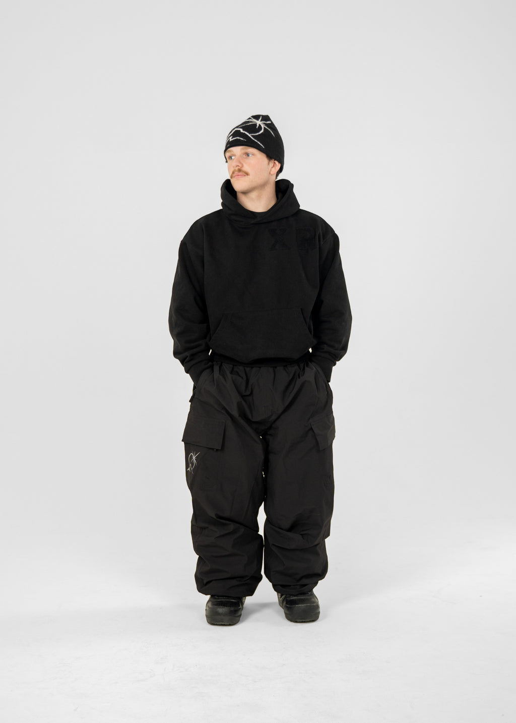 Person wearing a black Polar Pursuit  snowsuit and Polar Pursuit hat on a white background (Tom is 160cm 68kg wearing size M)